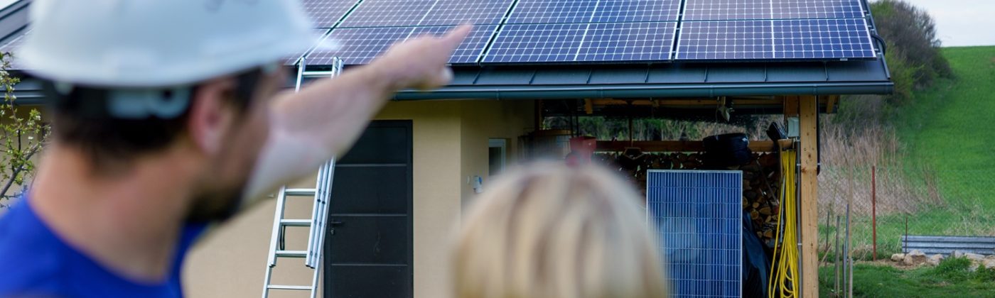 A man and woman solar installers engineers with tablet while installing solar panel system on house, rear view.