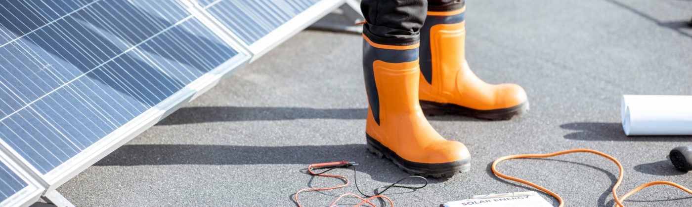 Installing solar panels, close-up on a working tools. wires and man in protective clothing standing on a rooftop with photovoltaic power station